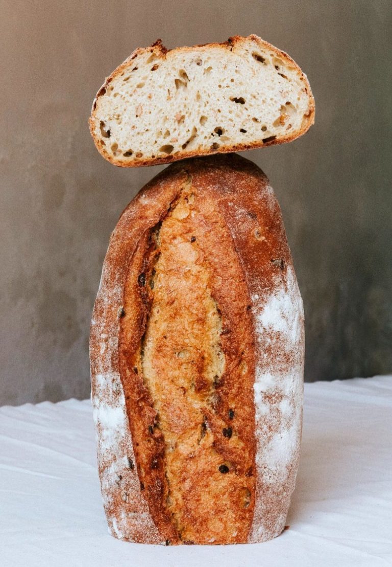 Pan de masa madre con corteza crujiente y miga clara, con un trozo encima.