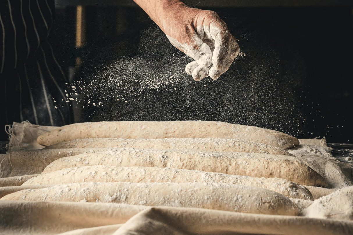 Masa de barras de pan lista para hornear Mano espolvoreando harina sobre masa en una superficie de trabajo para elaborar barras de pan artesano.