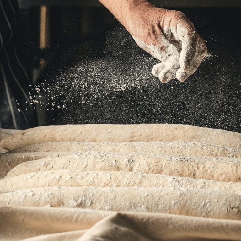 Mano espolvoreando harina sobre masa de pan en una superficie de trabajo.
