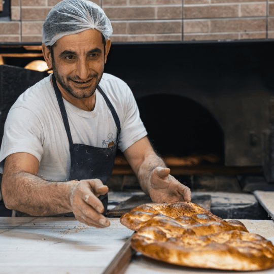 Panadero sonriente sirviendo pan recién horneado en una panadería.