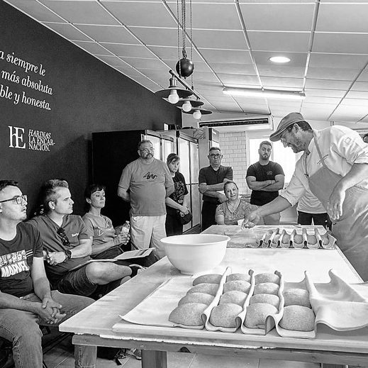 Javier Moreno realiza un taller demostración a un grupo de panaderos artesanos en un obrador con mesas y utensilios de panaderia.