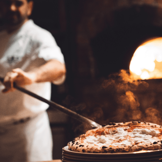 Chef sacando una pizza del horno de leña con una pala.