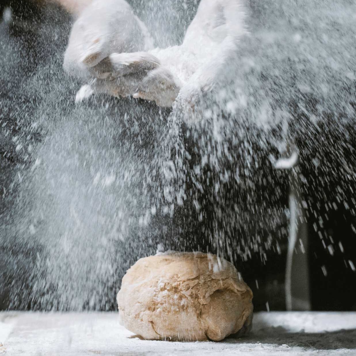 Manos espolvoreando harina SIN GLUTEN sobre una bola de masa en una superficie de trabajo .